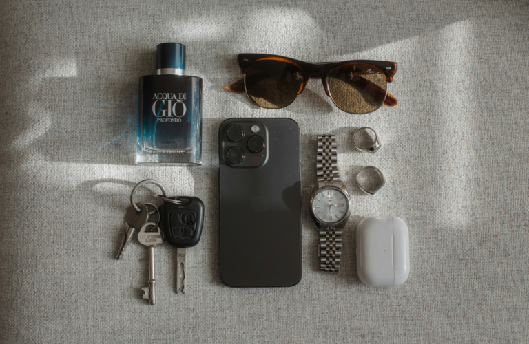 Flat lay of thoughtful gifts for men including headphones watch sunglasses and cologne on neutral background