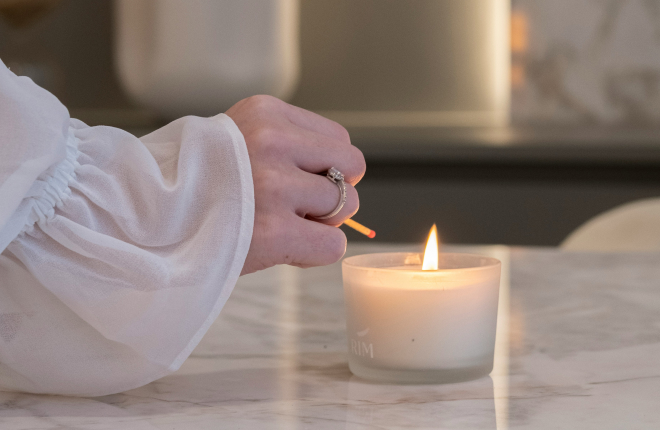 woman in white lighting a candle on marble surface slow living ritual
