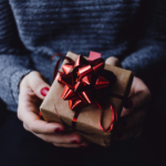 Flat lay of thoughtful gifts for women including perfume candle jewellery lip oil and polaroid camera on cream background