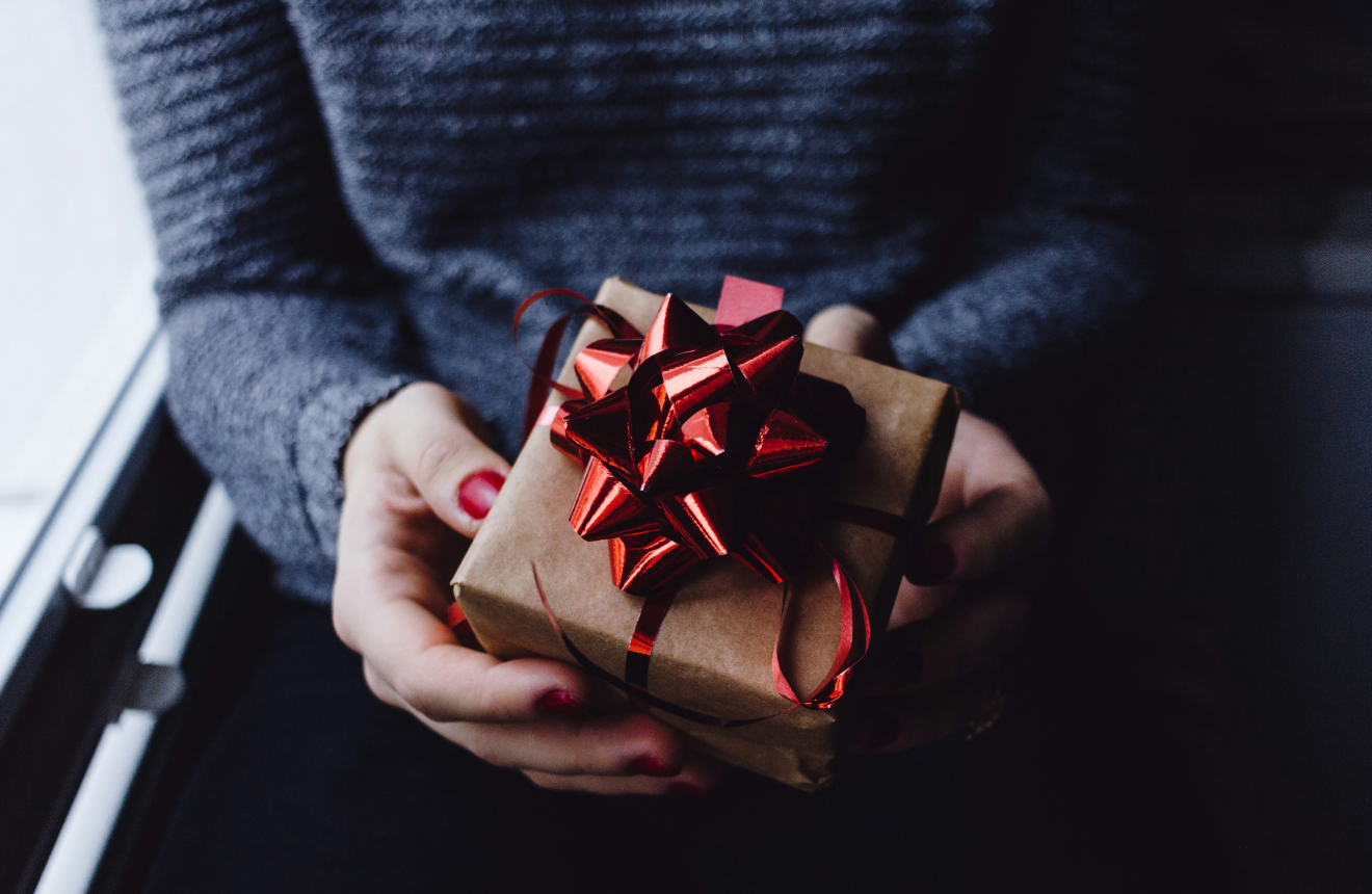 Flat lay of thoughtful gifts for women including perfume candle jewellery lip oil and polaroid camera on cream background